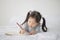 Little Asian girl lying on bed and writing alphabet on notebook