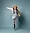 Little asian girl in shirt dress, double sided jacket, brown beret, boots. Laughing, jumping up on blue background. Full length