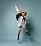 Little asian girl in shirt dress, double sided jacket, brown beret, boots. Laughing, jumping up on blue background. Full length