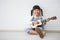 little asian girl sitting playing ukulele on white background with copy space