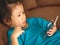 Little Asian kid using smartphone on sofa bed look concentrate to content. Using smartphone for children could effect them.
