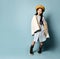 Little asian schoolgirl in shirt dress, double sided jacket, brown beret, boots. Smiling, posing on blue background. Full length