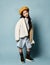 Little asian schoolgirl in shirt dress, double sided jacket, brown beret, boots. Smiling, posing on blue background. Full length