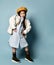 Little asian schoolgirl in shirt dress, double sided jacket, brown beret, boots. Smiling, posing on blue background. Full length