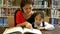 Little Asian students and teacher reading book in library together