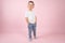 Little attractive boy posing, pink wall on background. Serious kid holding his hands in pockets.