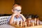 Little baby boy with down syndrome with big blue glasses playing chess in kindergarten