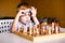 Little baby boy with down syndrome with big blue glasses playing chess in kindergarten