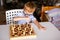 Little baby boy with down syndrome with big blue glasses playing chess in kindergarten