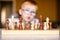 Little baby boy with down syndrome with big blue glasses playing chess in kindergarten