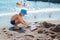 Little baby boy playing on the beach by the sea in sand and stones. Build sand castles.