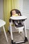 Little baby boy sitting in chair for feeding and eating special biscuit for babies. Kitchen