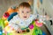 Little baby boy sitting in a colourful baby Walker with toys and