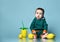 Little baby boy in stylish casual clothing barefoot sitting on floor and licking fresh yellow lemon fruit over blue background