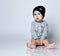 Little baby boy toddler in grey casual jumpsuit, cap and barefoot sitting on floor and smiling with raised hands