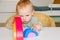 Little baby child in clothes made of natural fabric plays with rainbow colored wooden toys at white table. Cozy room