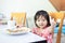 Little baby child showing thumb up, eating and enjoy breakfast by herself