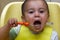 Little baby eats with a spoon soup plate. He sits on a children`s chair, putting foods