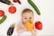 Little baby girl 6 months old sitting on the bed in the nursery with vegetables, baby`s first feeding, baby food concept, place