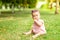 Little baby girl 7 months old sitting on the green grass in a pink bodysuit and bright glasses, walking in the fresh air