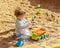Little baby girl Caucasian boy plays in the sandbox with a toy car. A child in a striped t-shirt pours sand into a truck with a