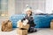 Little baby girl is folding up a mountain of gift boxes at home, near the bed. The interior is decorated with Christmas decor. Day