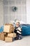 Little baby girl is folding up a mountain of gift boxes at home, near the bed. The interior is decorated with Christmas decor. Day