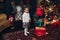 Little baby girl next to the fireplace with Christmas tree.