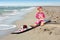 Little baby girl on the sand beach with surf board