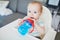 Little baby girl sitting in high chair and drinking water from sippy cup