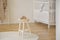 Little baby shoes placed on wooden stool standing in white kid room interior with crib, round rug and herringbone pa