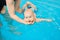 Little baby swimming in water pool with help from mothers hands