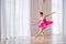 A little ballerina in a bright crimson tutu dances in a large light hall