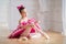 Little ballerina in a bright pink tutu sits on the floor in a bright hall and puts on pointe shoes