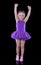 Little ballerina girl in a purple tutu dancing in a dark room