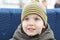 Little beautiful caucasian baby boy with bright blue eyes smiling, outdoors. Casual autumn, spring wear, yellow striped hat.