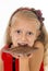Little beautiful female child in red dress holding happy delicious chocolate bar in her hands eating delighted