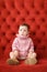 Little beautiful female child sitting on sofa with red background.