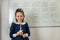 Little beautiful girl answers in front of the school blackboard smiling.