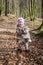 Little beautiful girl in a baby raincoat, hat and scarf is played in spring forest dry leaf litter throwing their smiles in a good