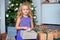 Little beautiful girl with blond curly hair considers her gifts against the background of the Christmas tree. Christmas