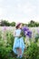 Little beautiful girl in a hat and dress stands in a field of lupins. Girl holds a large bouquet of purple lupins in a flowering f