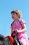 Little beautiful girl in pink dress sits on brown hors