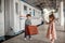 Little beautiful girl in retro dress says goodbye at the station with a little boy in vintage clothes with retro suitcase