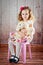 Little beautiful girl is sitting on a chair with a bear in her arms. Shot in a photo studio on a wooden background