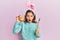 Little beautiful girl wearing cute easter bunny ears holding colored egg afraid and shocked with surprise and amazed expression,