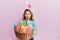 Little beautiful girl wearing cute easter bunny ears holding wicker basket with colored eggs afraid and shocked with surprise and