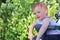 little, beautiful, smiling, cute redhead baby in a sleeveless shirt in a pram out-of-doors drops hands down and looking forward