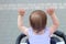 little, beautiful, smiling, cute redhead baby in a sleeveless shirt in a pram out-of-doors raises his hands up looking forward