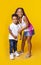 Little black sister hugging her toddler brother on yellow background